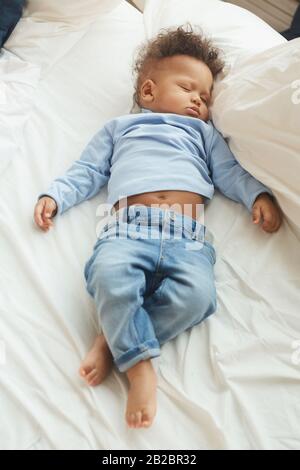 Blick oben auf das niedliche Mixed-Race-Baby, das auf einem bequemen Bett in weißen Bettlaken schläft Stockfoto