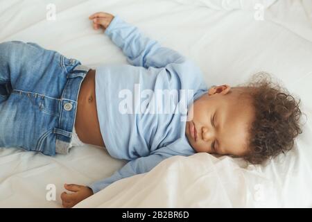 Hochwinkeliger Blick auf das niedliche Mixed-Race-Baby, das auf einem bequemen Bett in weißen Bettlaken schläft Stockfoto
