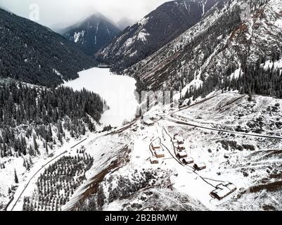 Luftbild zum Bergsee Kolsay und Dorfhäuser zur Winterzeit in den Bergen Kasachstans. Drohnenschuss, Draufsicht. Stockfoto