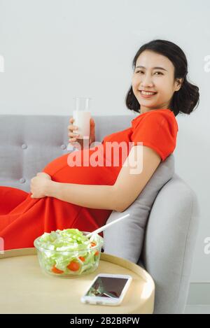 Junge schwangere Frau, die mit Salat und Milch frühstücken kann. Stockfoto