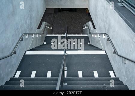 Weiße Markierungen, die auf blinde und sehbehinderte Menschen hinweisen, sind ein Landewechsel auf der Treppe eines Leman-Express-Bahnhofs in Genf, Schweiz Stockfoto