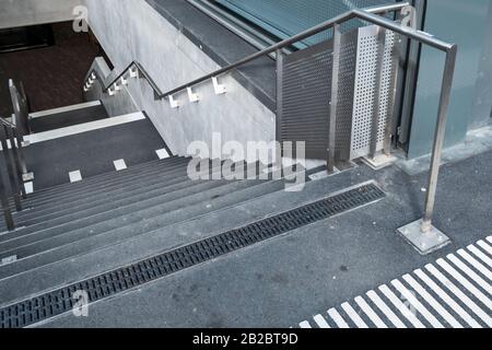 Weiße Markierungen, die auf blinde und sehbehinderte Menschen hinweisen, sind ein Landewechsel auf der Treppe eines Leman-Express-Bahnhofs in Genf, Schweiz Stockfoto