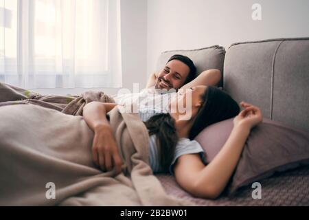 Junges glückliches Paar liegt morgens im Bett und spricht. Stockfoto