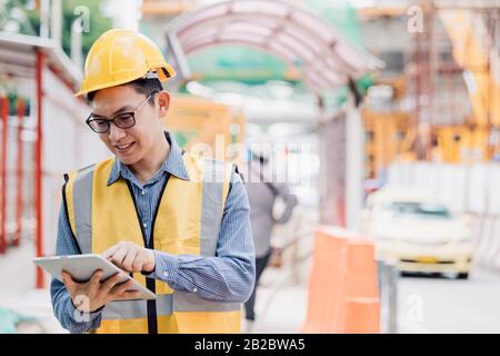 Bild außerhalb der Industriebauingenieure in gelbem Schutzhelm diskutieren über neues Projekt beim Einsatz von Laptop und fröhliches Lächeln auf dem offenen Bui Stockfoto