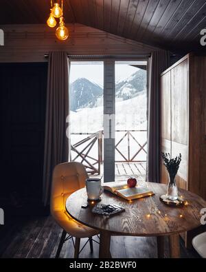 Loft-Inneneinrichtung mit warmen Lichtern in einem Winter-Cottage aus Holz mit schönem Blick auf die Berge Stockfoto