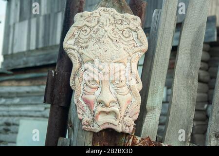 Alte afrikanische alten handgemachten Maske auf hölzernen Zaun in der Nähe von House. Die afrikanische Kultur traditionelle Masken Nahaufnahme Stockfoto