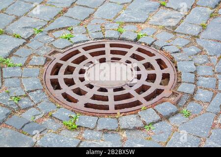 Kanaldeckel in der Nähe von Pflastersteinen. Rusty Kanaldeckel auf dem Walkside mit Pflastersteinen Stockfoto