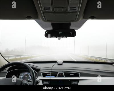 Im Nebel geht das Auto schnell auf die Straße, vom Fahrgastraum aus gesehen. Stockfoto