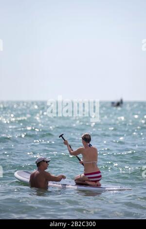 Ein Paar im Wasser in Florida, lernen, wie man ein SUP Stand Up Paddle Board verwendet. Für Wassersportaktivitäten. Stockfoto