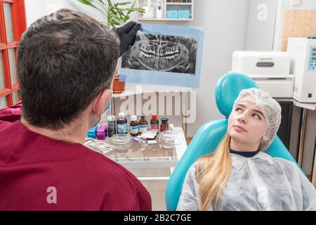 Der Zahnarztarzt untersucht ein Röntgenbild der Zähne, die in der Nähe eines Patienten sitzen Stockfoto