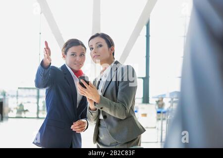 Passagier-Servicemitarbeiter, die Geschäftsfrau beim Flughafen unterstützen und Wegbeschreibungen geben Stockfoto