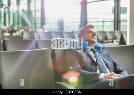 Reifer Geschäftsmann, der mit seinem Kissen sitzt und schläft, während er auf das Einsteigen in den Flughafen wartet Stockfoto