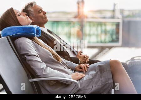 Reifer Geschäftsmann und junge attraktive Geschäftsfrau, die während des Wartens auf das Einsteigen in ihr Flugsteig am Flughafen schläft Stockfoto