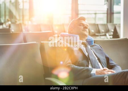 Reifer Geschäftsmann, der mit seinem Kissen sitzt und schläft, während er auf das Einsteigen in den Flughafen wartet Stockfoto