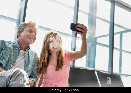 Porträt des jungen schönen Teenager-Mädchens, das selfie mit ihrem Vater auf dem Flughafen nimmt Stockfoto