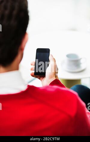 Geschäftsmann, der Smartphone verwendet, während er in der Lobby sitzt und Kaffee trinkt Stockfoto