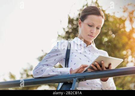 Portrait junger attraktiver Geschäftsfrau mit digitalem Tablet, während sie sich auf Geländer stützt Stockfoto