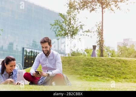 Geschäftsleute, die Smartphone nutzen, während sie auf dem Gras sitzen Stockfoto