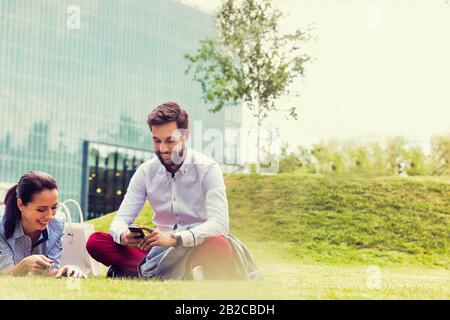 Geschäftsleute, die Smartphone nutzen, während sie auf dem Gras sitzen Stockfoto