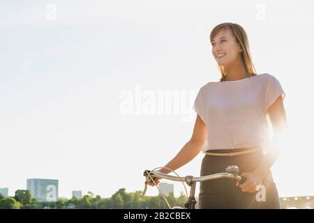 Porträt der jungen attraktiven Geschäftsfrau, die beim Strandspaziergehen Fahrrad hält Stockfoto