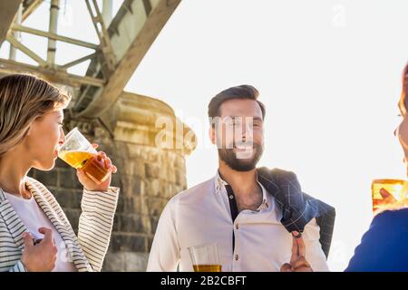 Geschäftsleute feiern Erfolg, während sie Bier am Strand mit Linsenflauge im Hintergrund trinken Stockfoto