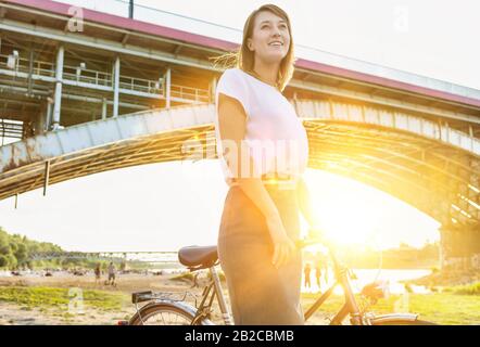 Porträt der jungen attraktiven Geschäftsfrau, die Fahrrad hält, während sie unter der Brücke spazieren geht Stockfoto