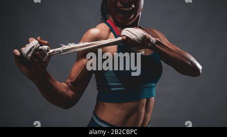 Nahaufnahme des athletischen, gesunden, mageren Oberkörpers der asiatischen Frau, die einen weißen Gurt mit beiden Händen hält, die sich auf das Training oder Boxen vorbereiten, während sie auf die Seite schauen Stockfoto