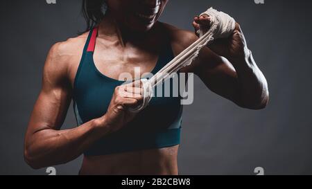 Nahaufnahme des athletischen, gesunden, mageren Oberkörpers der asiatischen Frau, die einen weißen Gurt mit beiden Händen hält, die sich auf das Training oder Boxen vorbereiten, während sie auf die Seite schauen Stockfoto