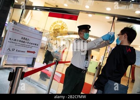 Macao, China. März 2020. Ein Mitarbeiter testet die Körpertemperatur eines Kunden in einer Filiale der Bank of China in Macao, Südchina, 2. März 2020. Credit: Cheong Kam Ka/Xinhua/Alamy Live News Stockfoto