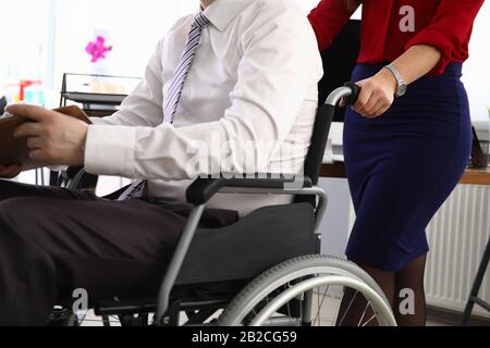 Frau trägt Mann im Anzug am Rollstuhlarbeitsplatz Stockfoto