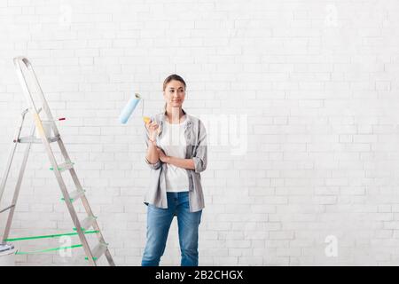 Junge Frau, die eine Walze zum Malen von Wänden in einem neuen Haus hält Stockfoto