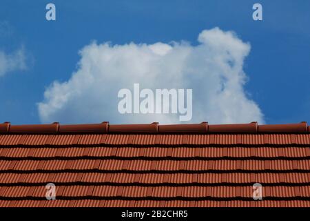 Modernes hellbraun-rotes Lehmziegel schiefergedecktes Wohndach und Lehm. Klarer blauer Himmel und weiße Wolken. Baukonzept. Moderne Dachdeckmaterialien Stockfoto