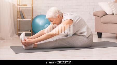 Aktive Seniorin macht Dehnübungen zu Hause Stockfoto