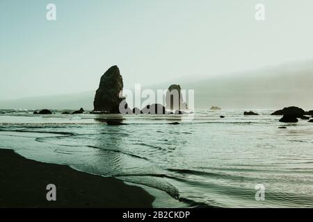 Cannon Beach ist eine kleine Küstenstadt im Nordwesten von Oregon. Es ist bekannt für sein langes, sandiges Ufer. Der Haystack Rock, der hoch im Ozean steht, ist eine Würfelgruppe Stockfoto