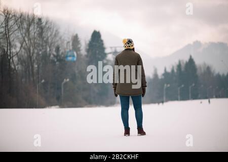 Frau auf der Skipiste mit Blick auf die Berglandschaft. Blick von hinten auf ein Mädchen, das auf der Skipiste steht und in den verschneiten Berg blickt. Stockfoto