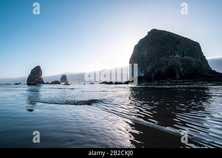 Cannon Beach ist eine kleine Küstenstadt im Nordwesten von Oregon. Es ist bekannt für sein langes, sandiges Ufer. Der Haystack Rock, der hoch im Ozean steht, ist eine Würfelgruppe Stockfoto
