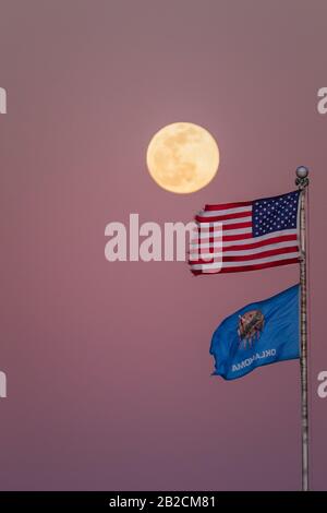 Ein schöner Vollmond, der über die amerikanische und Oklahoma Flag steigt, während die Sonne untergeht. Stockfoto