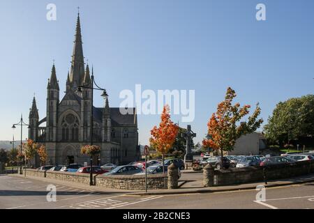 Sonniger Herbsttag am Cathedral Square in Letterkenny, Irland mit modernem Hochkreuz auf dem Parkplatz und der St Eunan's Cathedral im Hintergrund. Stockfoto