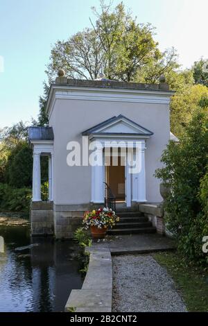 Steinpfad am Seeufer zu einer modernen Grotte, Dem Nymphaeum am Ovalsee im Herbst im Oakfield Park, Raphoe, County Donegal. Stockfoto