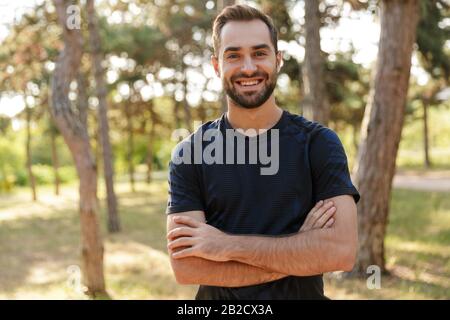 Bild eines jungen, starken fröhlichen Sportmannes, der im Freien im grünen Park posiert. Stockfoto