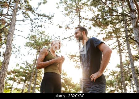 Foto des jungen attraktiven Paares in der Sportbekleidung Lachen beim Ausarbeiten im grünen Park während des sonnigen Sommertags Stockfoto