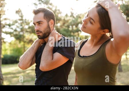 Bild einer jungen, stark konzentrierten Sportfrau und eines Mannes machen Dehnübungen im Freien im grünen Park. Stockfoto