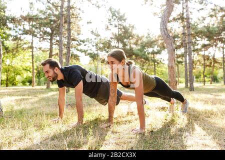 Bild einer jungen starken fröhlichen Sportlerin und eines Mannes machen im grünen Park Push-ups im Freien. Stockfoto