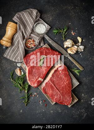 Zwei Rohe Frische Steaks Mit Rosemary, Knoblauch und Gewürzen auf Holzschneidebrett. Schwarzes Angus-Rind-Fleisch. Draufsicht Stockfoto
