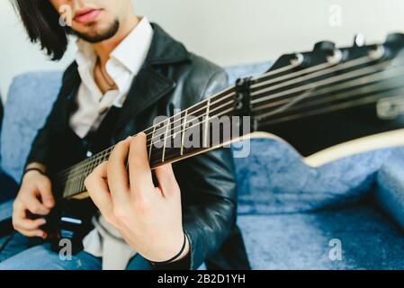 Junger Mann, der mit seiner E-Gitarre auf dem Sofa seines Hauses lernen. Stockfoto
