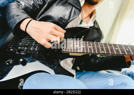 Junger Mann, der mit seiner E-Gitarre auf dem Sofa seines Hauses lernen. Stockfoto