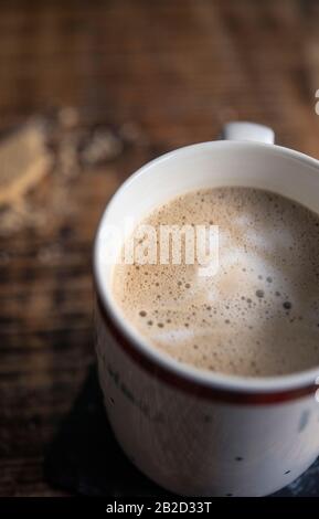 Becher mit milchigem Kaffee und Keksbröseln auf einem Holztisch Stockfoto