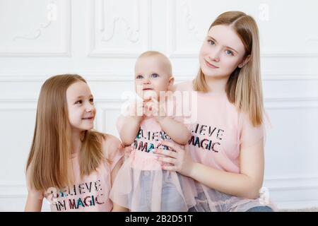 Serie Light Family. Drei Schwestern auf weißem Hintergrund, bekleidet mit lustigen T-Shirts und Jeans Stockfoto