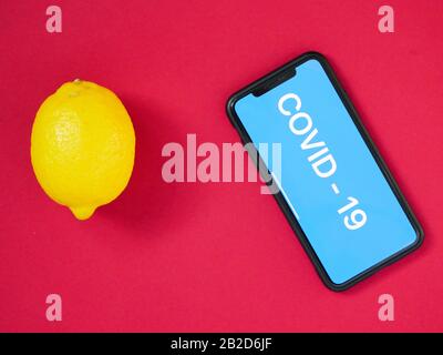 Zitrone und Smartphone mit der Aufschrift COVID - 19 auf farbigem Hintergrund. Vitamin C. Das Konzept der Behandlung des Virus Stockfoto