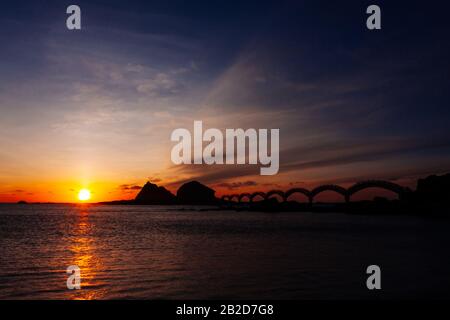 Eine kleine Insel vor der Küste und die berühmte Fußgängerbrücke mit acht Bögen, die bei Sonnenaufgang in Sanxiantai in Taitung, Taiwan, umrissen wurde Stockfoto